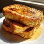 Close-up of a stack of thick, golden brown protein french toast drizzled with syrup.