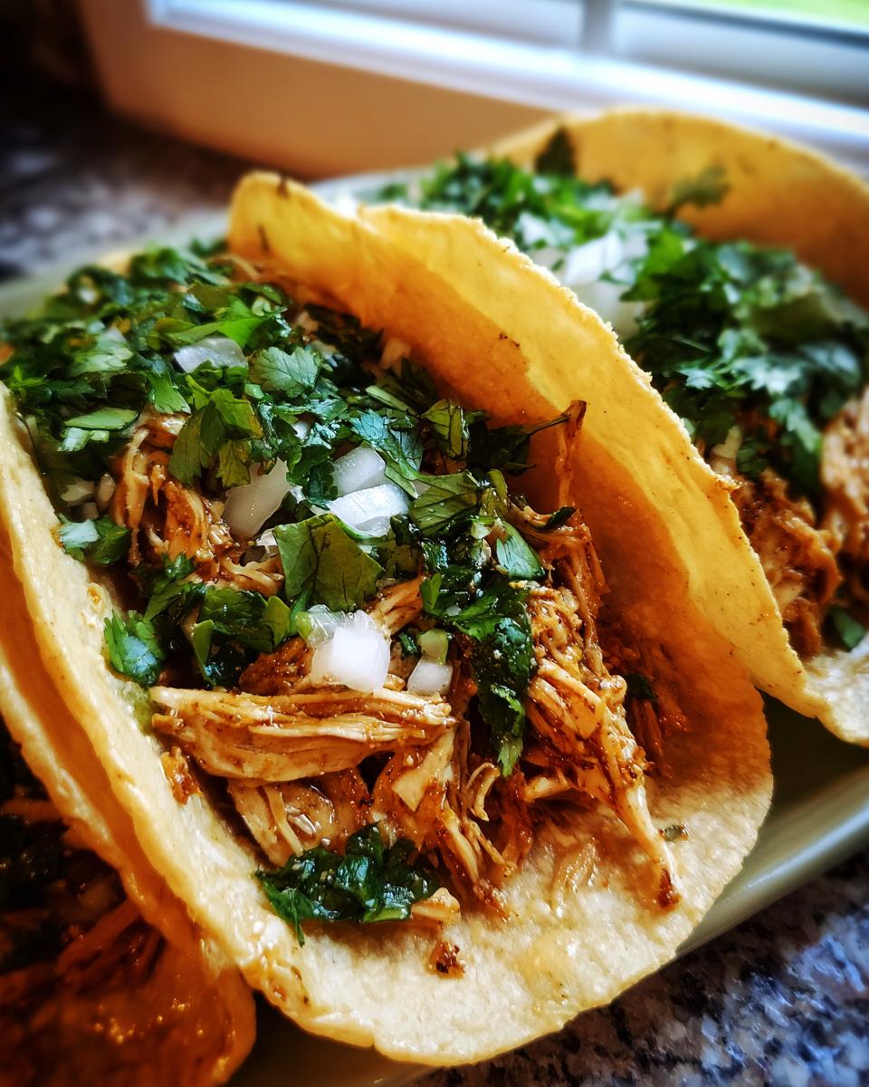 Close-up of two delicious chicken tacos filled with shredded seasoned meat, topped with fresh cilantro and diced white onion.