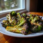 Close-up of perfectly charred and crispy smashed broccoli florets served on a white plate near a window.