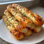 A stack of golden, soft breadsticks topped with melted cheese and fresh parsley, ready to eat.