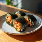 Four thick slices of homemade tuna kimbap, showing a vibrant orange spicy tuna filling wrapped in rice and dark seaweed (nori).
