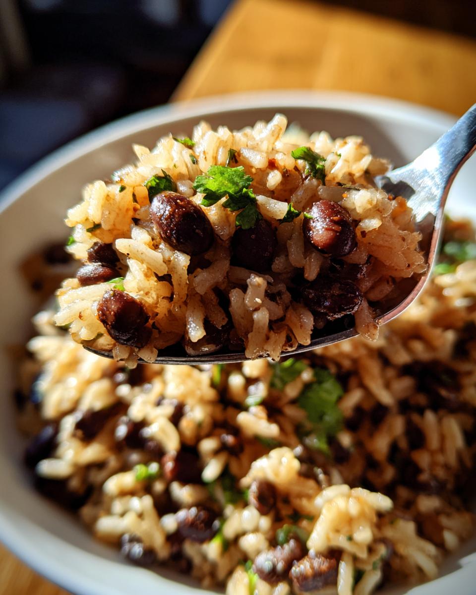 A spoonful of flavorful black beans and rice mixed with herbs, lifted above a bowl of the dish.