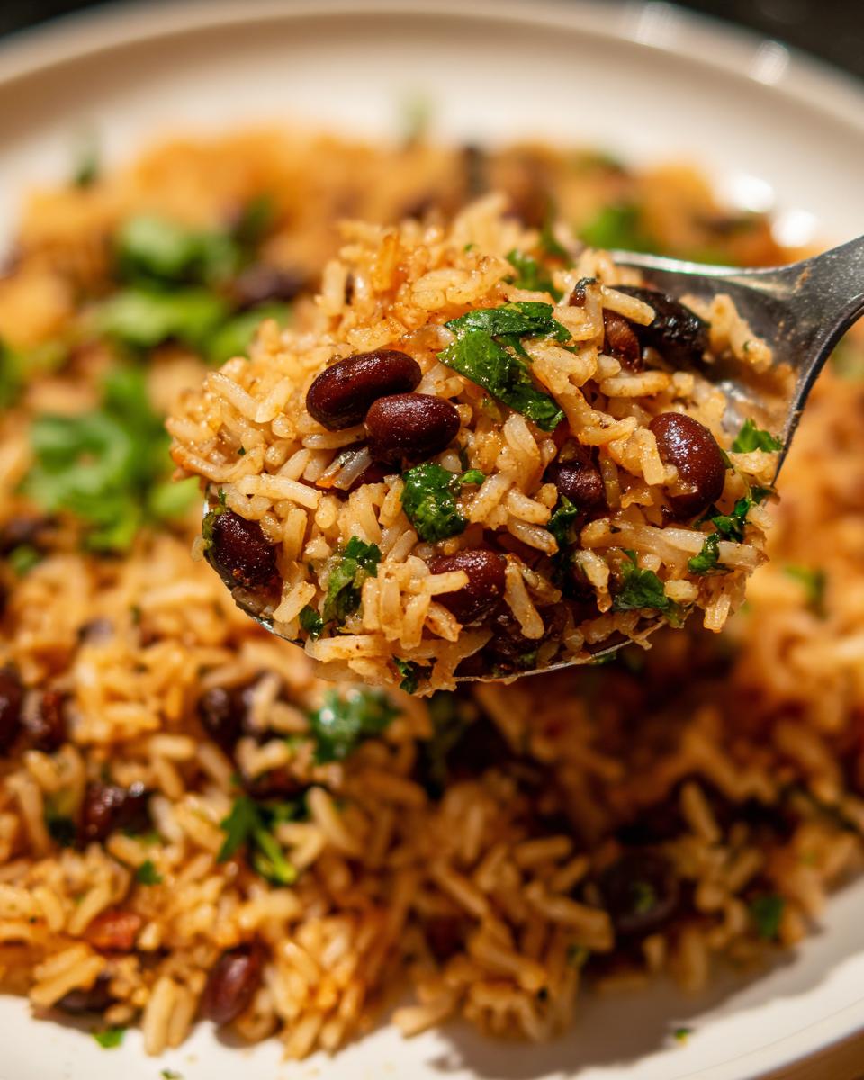 A close-up shot showing a spoonful of seasoned rice mixed with black beans and fresh cilantro, ready to eat from a plate of black beans and rice.