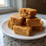 A stack of rich, light brown squares of homemade penuche fudge resting on a white plate.