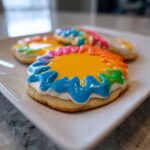 Close-up of a sugar cookie decorated with bright yellow icing and a rainbow border made from royal icing, showcasing the sugar cookie icing recipe.