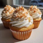 Close-up of three delicious coconut cupcakes topped with white frosting and toasted coconut flakes.