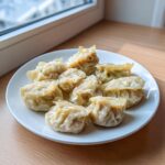 A plate of freshly steamed Traditional Chinese Dumplings arranged near a bright window.