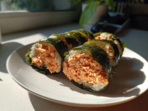 Several slices of homemade tuna kimbap, featuring creamy orange filling wrapped in rice and nori, resting on a white plate.