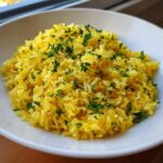 A close-up of fluffy, yellow mediterranean rice topped generously with chopped fresh parsley.