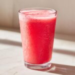 A tall, frosty glass filled with a vibrant red watermelon smoothie, covered in condensation.