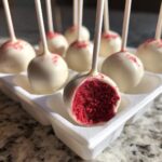 Close-up of white chocolate coated red velvet cake pops, one is bitten showing the bright red interior.
