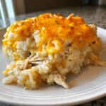 A close-up of a serving of creamy chicken and rice casserole topped with melted cheddar cheese.