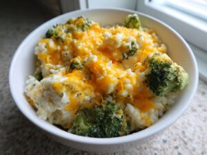 A close-up of a white bowl filled with creamy broccoli rice topped generously with melted cheddar cheese.