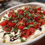 A close-up of a creamy base topped with halved cherry tomatoes, fresh basil, and a balsamic glaze, representing an amazing bruschetta dip.
