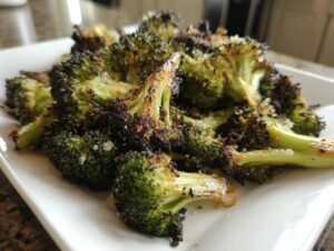 Close-up of crispy, charred roasted broccoli florets sprinkled with salt on a white serving dish.