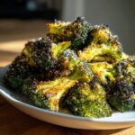 Close-up of perfectly roasted broccoli florets piled on a white plate, showing crispy edges and a dusting of Parmesan cheese.