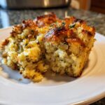 A close-up of a golden brown, savory slice of homemade stuffing on a white plate.