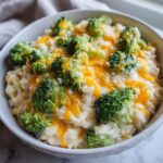 A close-up of creamy, cheesy broccoli rice topped with bright green florets and melted cheddar cheese.