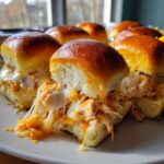 Close-up of gooey buffalo chicken sliders with shredded chicken and melted white cheese stretching between the buns.