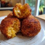 Close-up of golden-brown, crispy fried rice balls, one broken open showing a cheesy, gooey interior.