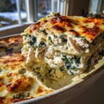 A generous slice of creamy chicken alfredo lasagna, layered with spinach and topped with browned cheese, being lifted from the baking dish.