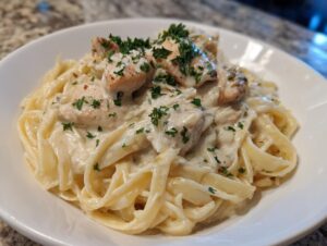 A close-up of a serving of rich chicken fettuccine alfredo pasta topped with grilled chicken pieces and fresh parsley.