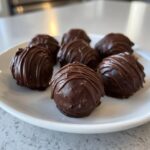 A close-up of several rich, chocolate-covered Oreo balls drizzled with extra chocolate, served on a white plate.