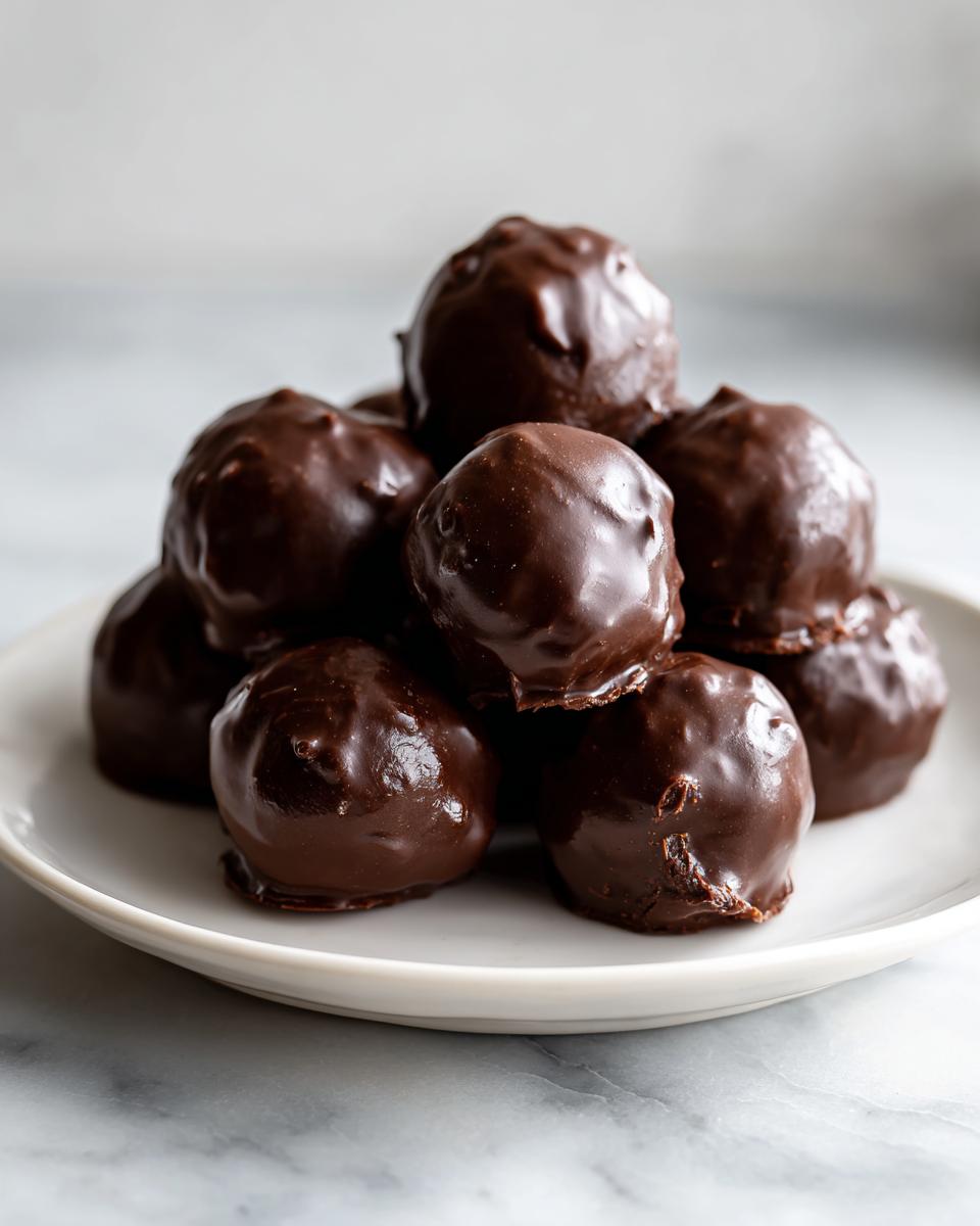 A stack of rich, dark chocolate-coated Oreo balls piled high on a small white plate.
