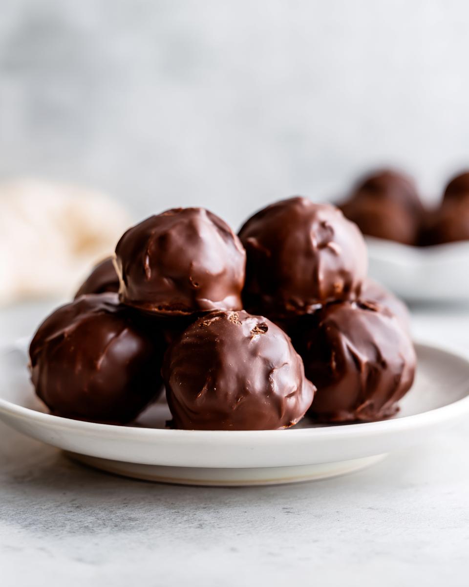 A close-up of several rich, chocolate-covered Oreo balls stacked on a small white plate.