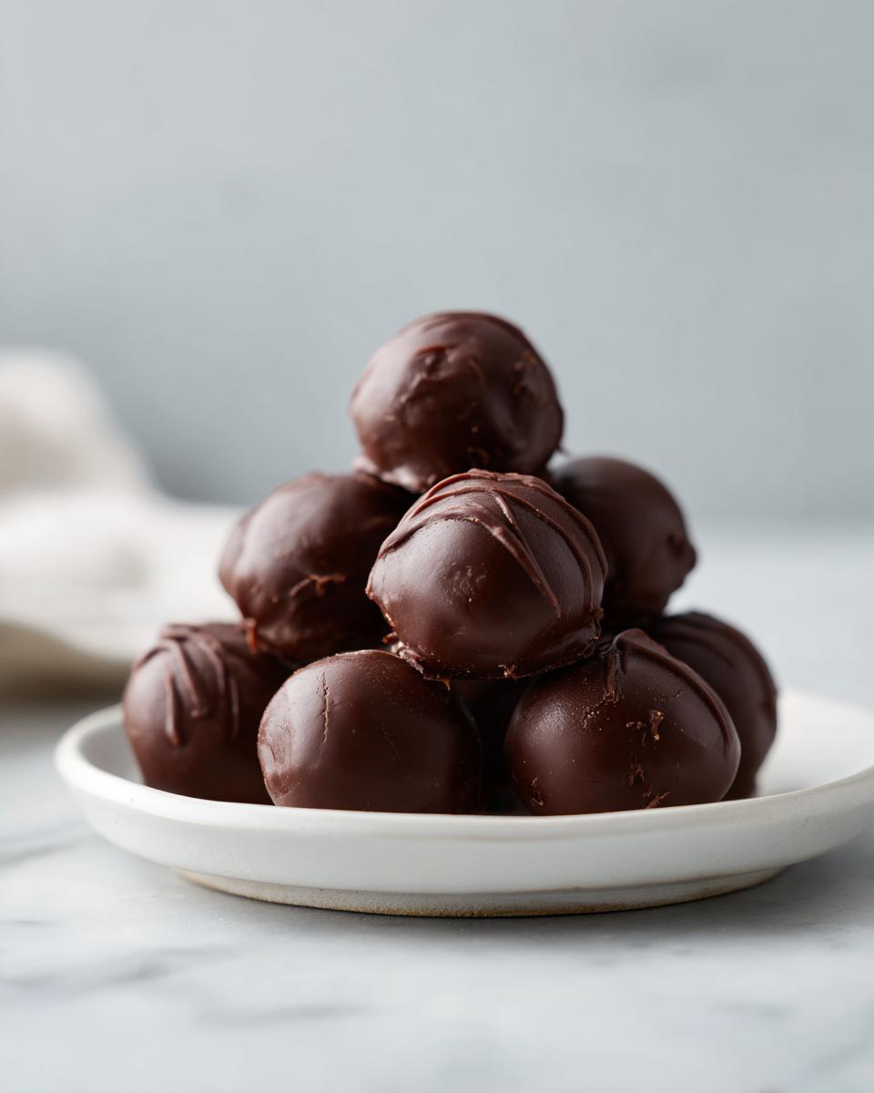 A stack of rich, dark chocolate coated oreo balls piled high on a small white plate.