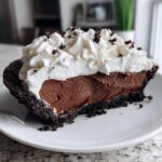A decadent slice of chocolate mousse pie with a dark crust, rich filling, and topped with whipped cream and cookie crumbs.