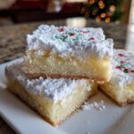Close-up of stacked Christmas gooey butter cookies squares topped with powdered sugar and red/green sprinkles.