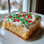 A close-up of a single serving of christmas sugar cookie bars topped with white frosting and red and green sprinkles.