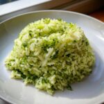 A perfectly molded mound of bright green cilantro lime rice served on a white plate, highlighted by natural light.