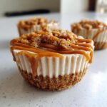 A close-up of a single cookie butter cheesecake cup topped with caramel sauce and cookie crumbs.