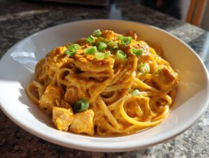 A white bowl filled with creamy cajun chicken pasta, featuring chunks of seasoned chicken and garnished with fresh sliced green onions.