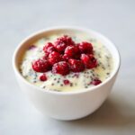 Close-up of creamy chia seed pudding mixed with vanilla liquid, topped generously with bright red raspberries.
