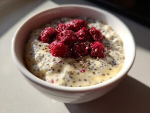 A white bowl filled with creamy chia seed pudding topped with bright red raspberries and sprinkled seeds.