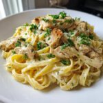 A close-up of creamy chicken fettuccine alfredo pasta topped with grilled chicken pieces and fresh parsley.