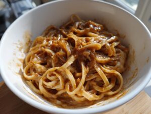 A close-up view of creamy french onion pasta coated in a rich, brown sauce, served in a white bowl.