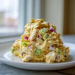 A scoop of creamy honey mustard chicken salad mixed with diced red onion and celery on a white plate.