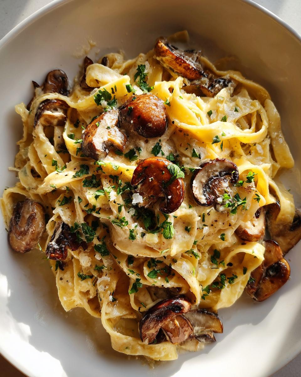 Close-up overhead shot of creamy fettuccine mushroom pasta topped with sautéed mushrooms and fresh parsley.