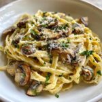 Close-up of creamy fettuccine pasta tossed with sautéed mushrooms, topped with Parmesan and parsley for an amazing mushroom pasta.