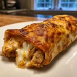 A close-up of a crispy, baked chicken chimichanga oozing with melted white cheese.