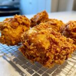 Close-up of several pieces of golden brown, extra crispy fried chicken resting on a wire cooling rack.