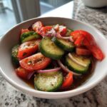 Close-up of a vibrant cucumber tomato salad with red onion slices tossed in a vinaigrette dressing.
