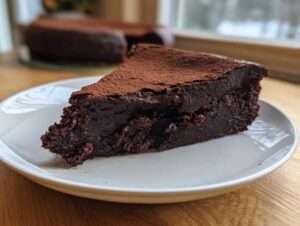 A decadent slice of flourless chocolate torte, intensely dark and fudgy, dusted with cocoa powder, resting on a white plate.