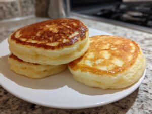 Close-up of three fluffy pancakes stacked and drizzled with syrup on a white plate, ready for breakfast.