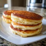 Close-up of three perfectly stacked, thick, fluffy pancakes with deeply golden brown tops, ready for breakfast.