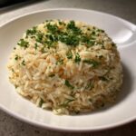 A perfectly molded serving of fluffy rice pilaf garnished generously with chopped fresh parsley.